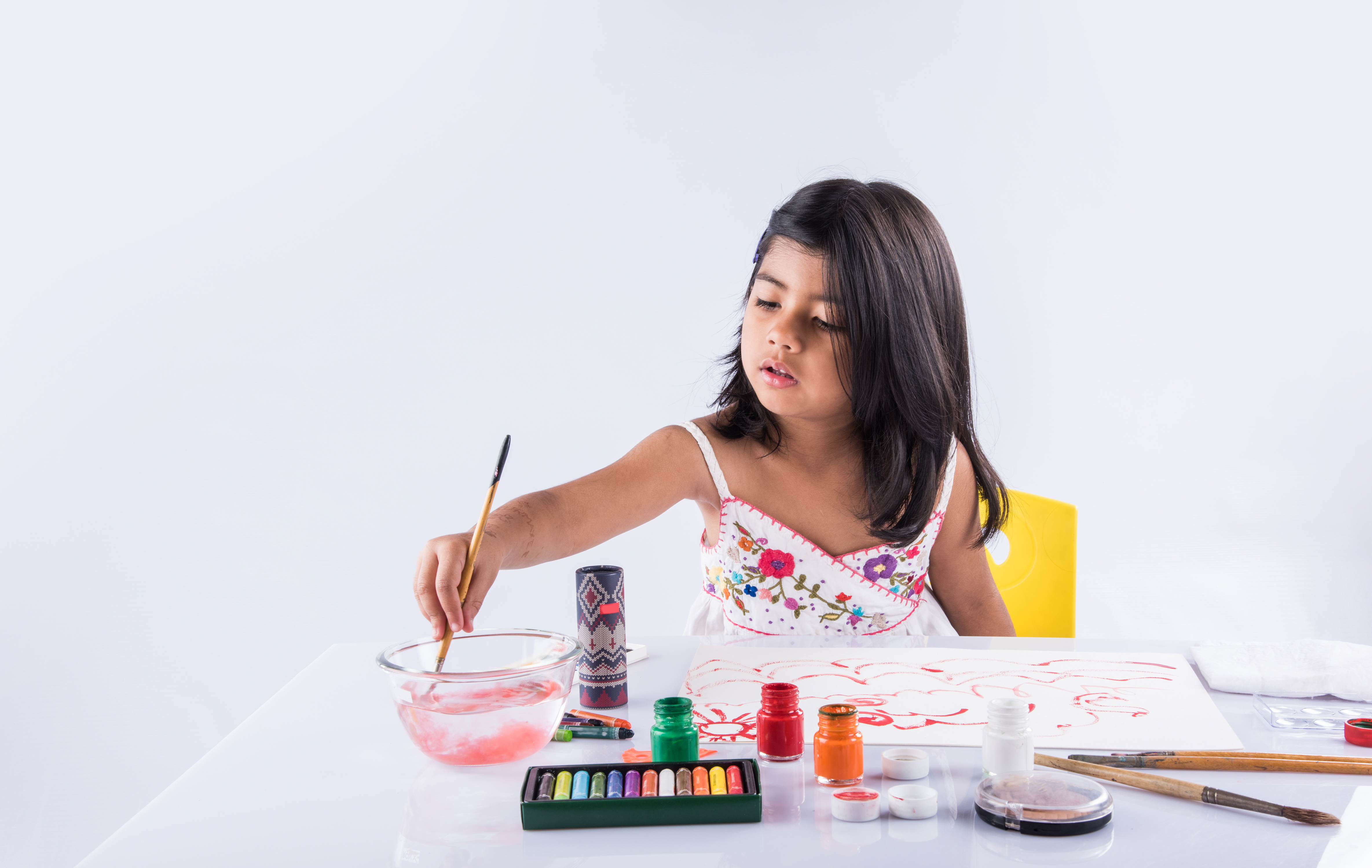 Young girl painting with a brush, surrounded by art supplies.