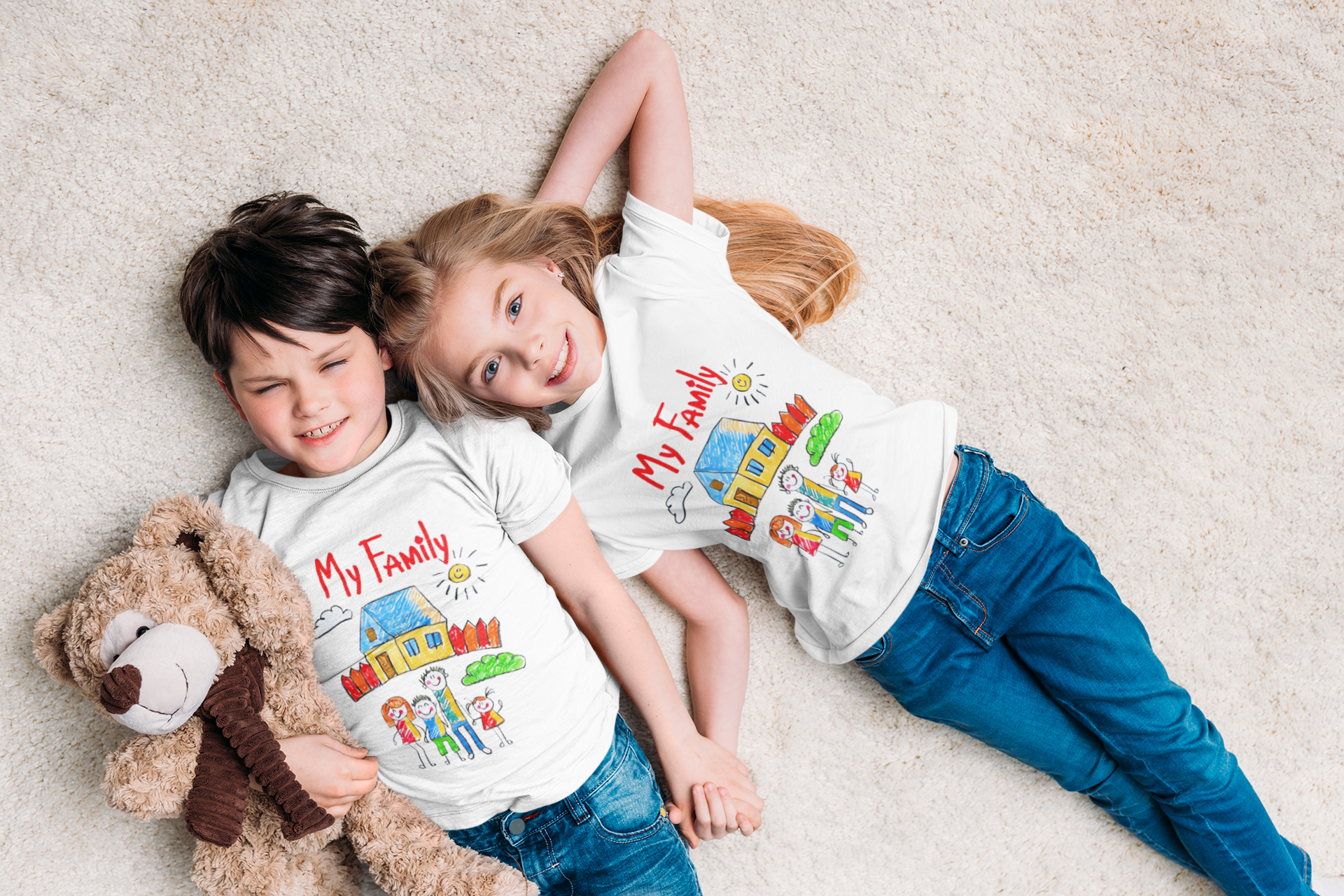 Two kids wearing matching "My Family" t-shirts lying on the floor holding a teddy bear.